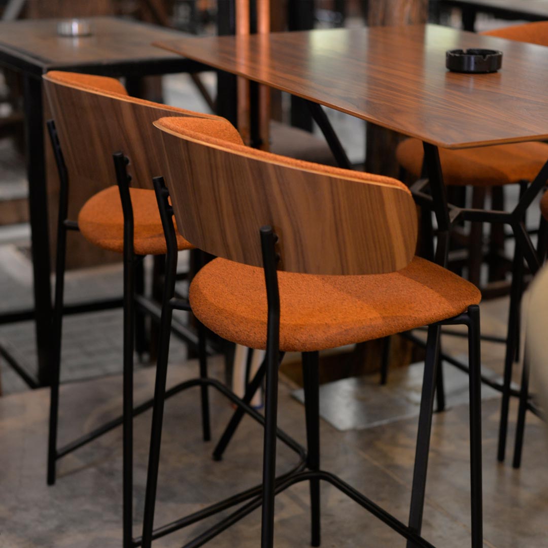 Bar chair in orange with walnut veneer seat and black metal legs in lounge bar.