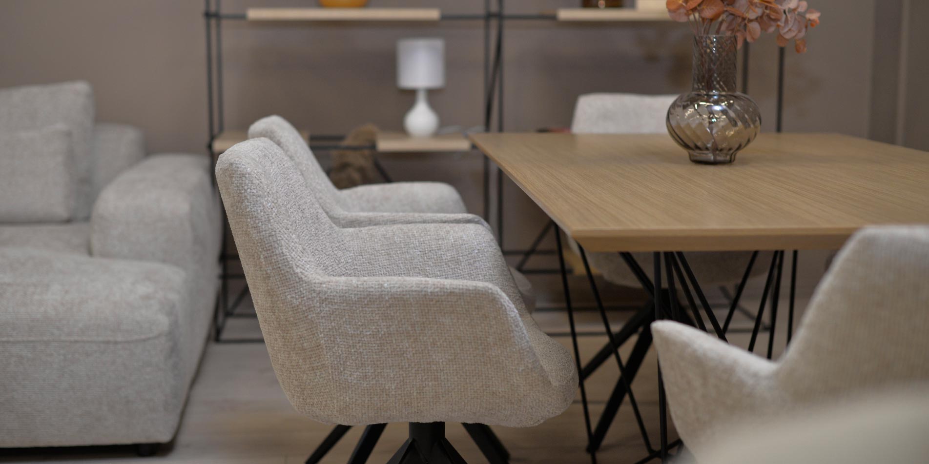 Dining chair in beige upholstery with black metal legs on dining table with oak top.