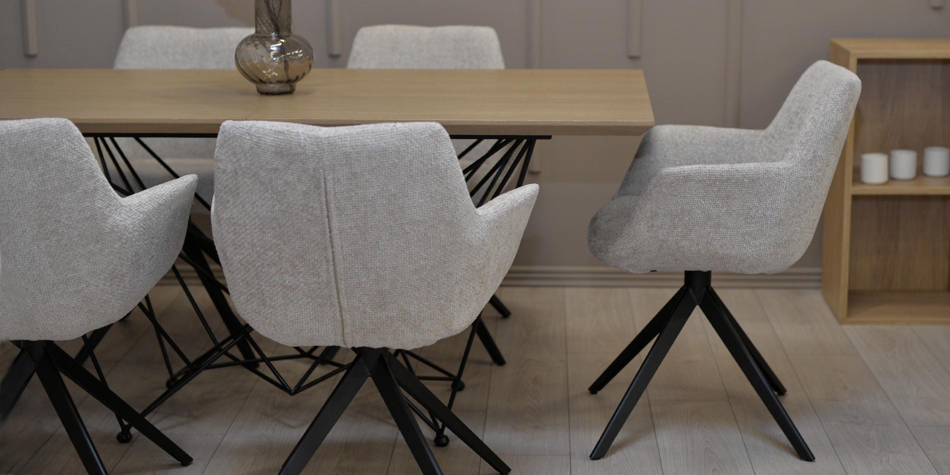 Dining chair in beige upholstery with black metal legs on dining table with oak top.