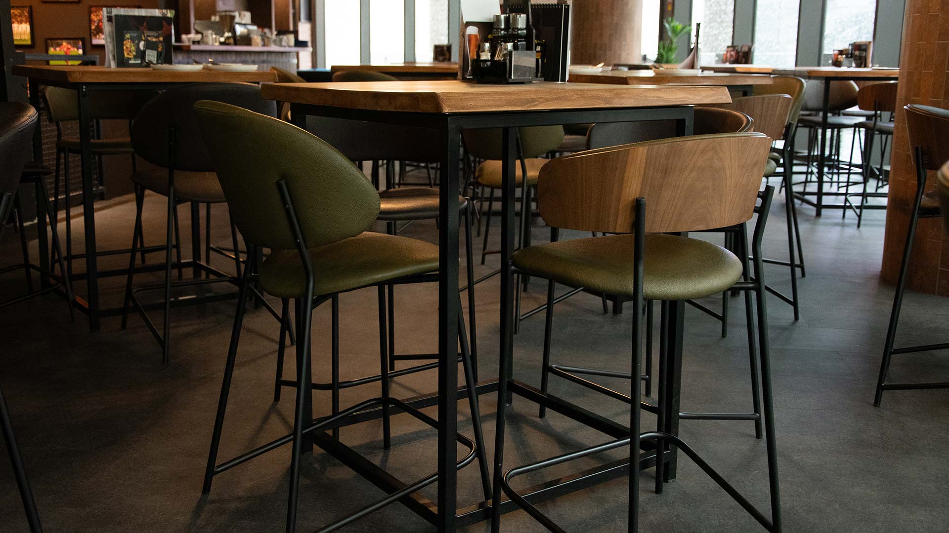 Два типа на барски столици со црни метални ногарки и зелена еко кожа, како дел од ентериерот на спортски бар.