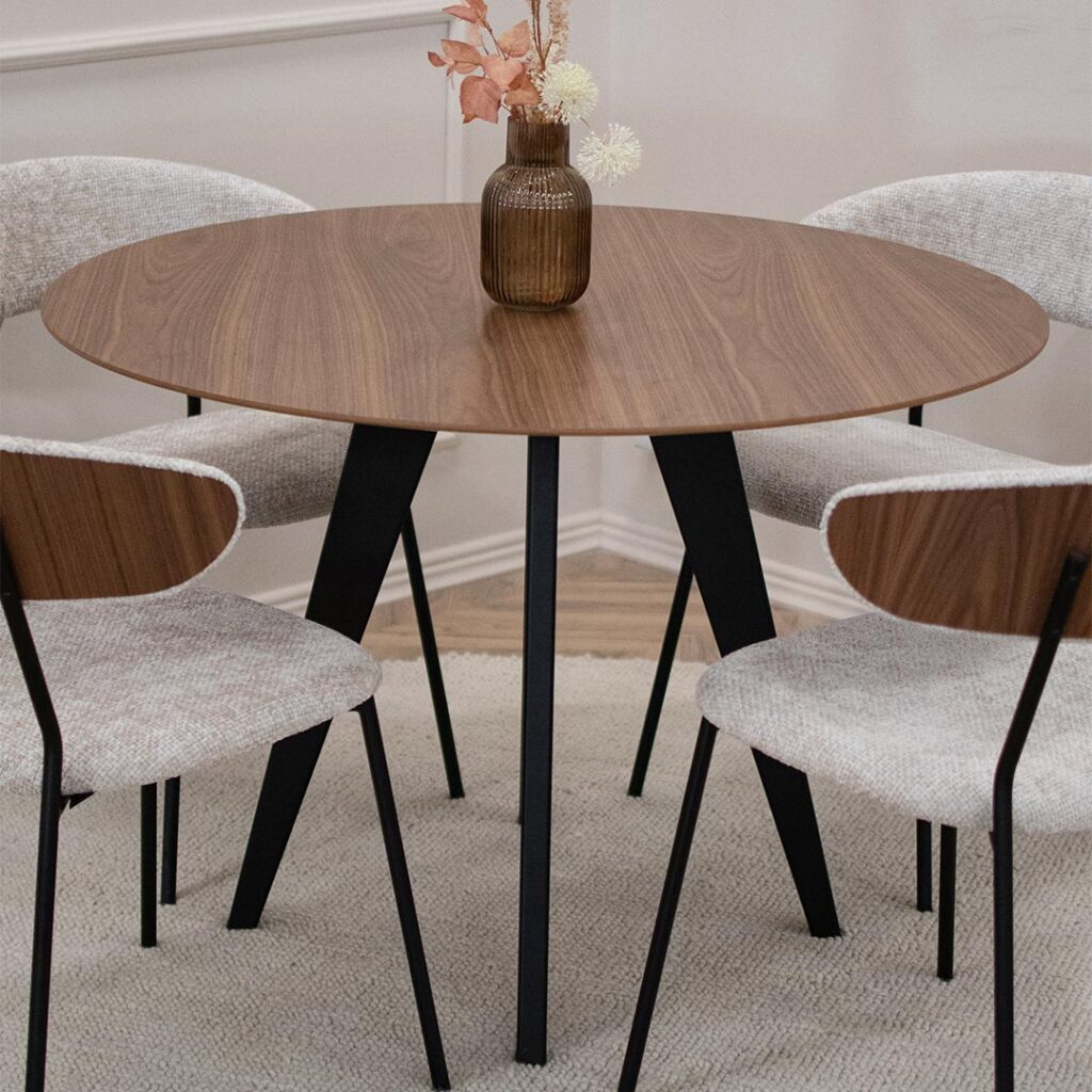 Мала кружна маса со плотна орев и црни ногарки, со 4 столици со метални ногарки и светло крем мебел штоф, кои на грб имаат фурнир од орев.