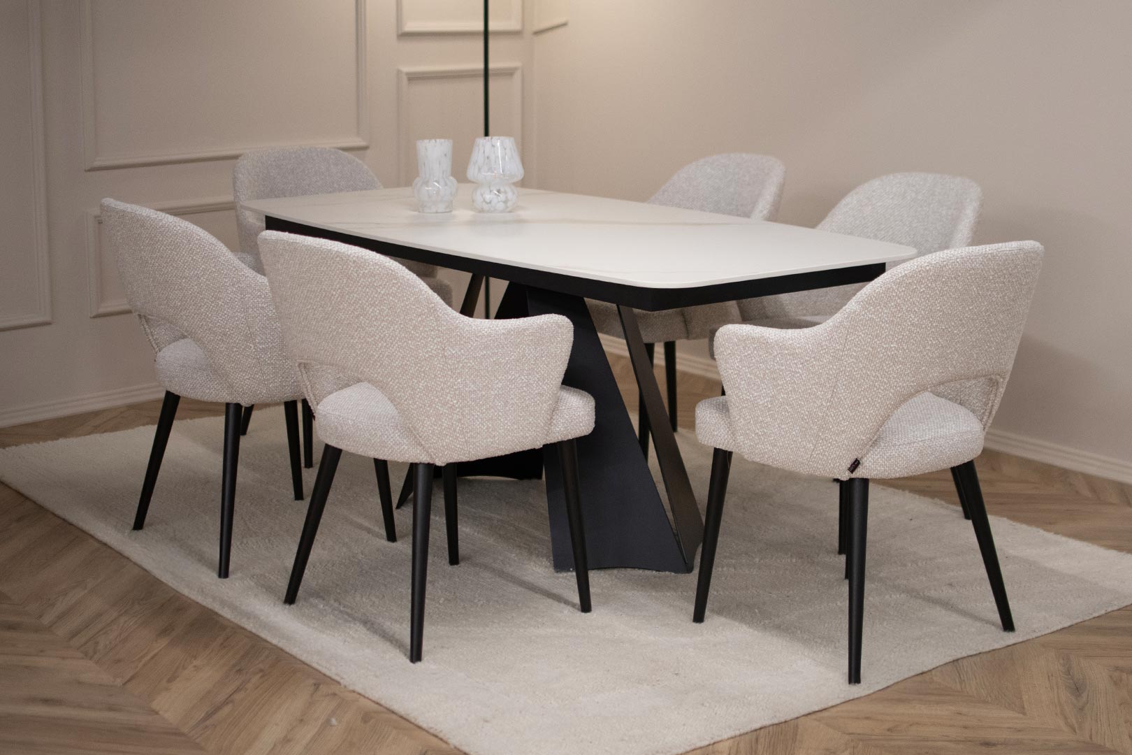 Трпезариска маса со керамичка плотна во бела боја со крем шари поставена на две црни метални ногарки во комбинација со столици со раконаслон во бел мебел штоф со црни дрвени ногарки.