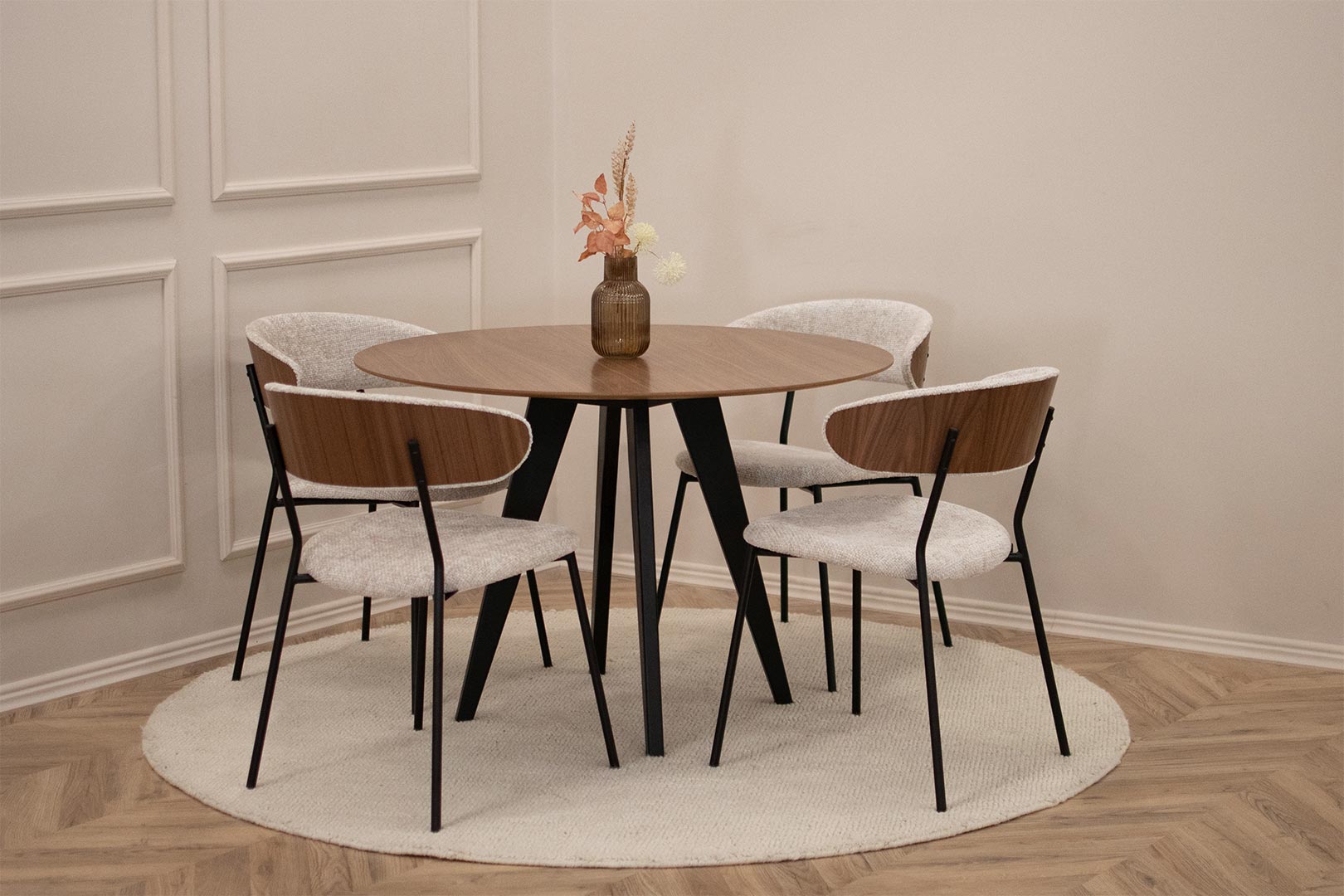 Мала кружна маса со плотна орев и црни ногарки, со 4 столици со метални ногарки и светло крем мебел штоф, кои на грб имаат фурнир од орев.