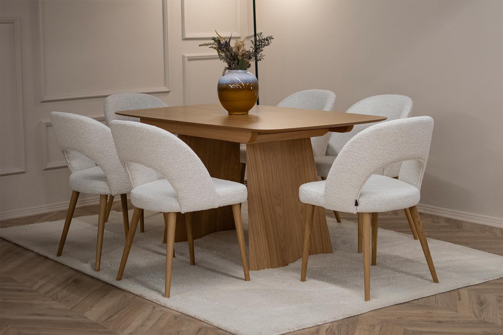 Трпезариски сет со маса Сфера од маслен даб со две неправилно обликувани ногарки во комбинација со 6 столици со даб ногарки и бел мебел штоф.
