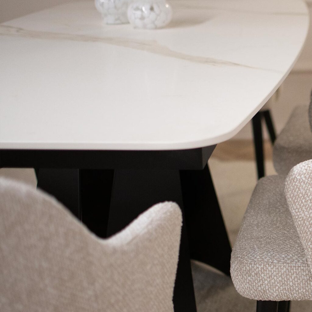 Трпезариска маса со керамичка плотна во бела боја со крем шари поставена на две црни метални ногарки во комбинација со столици со раконаслон во бел мебел штоф со црни дрвени ногарки.