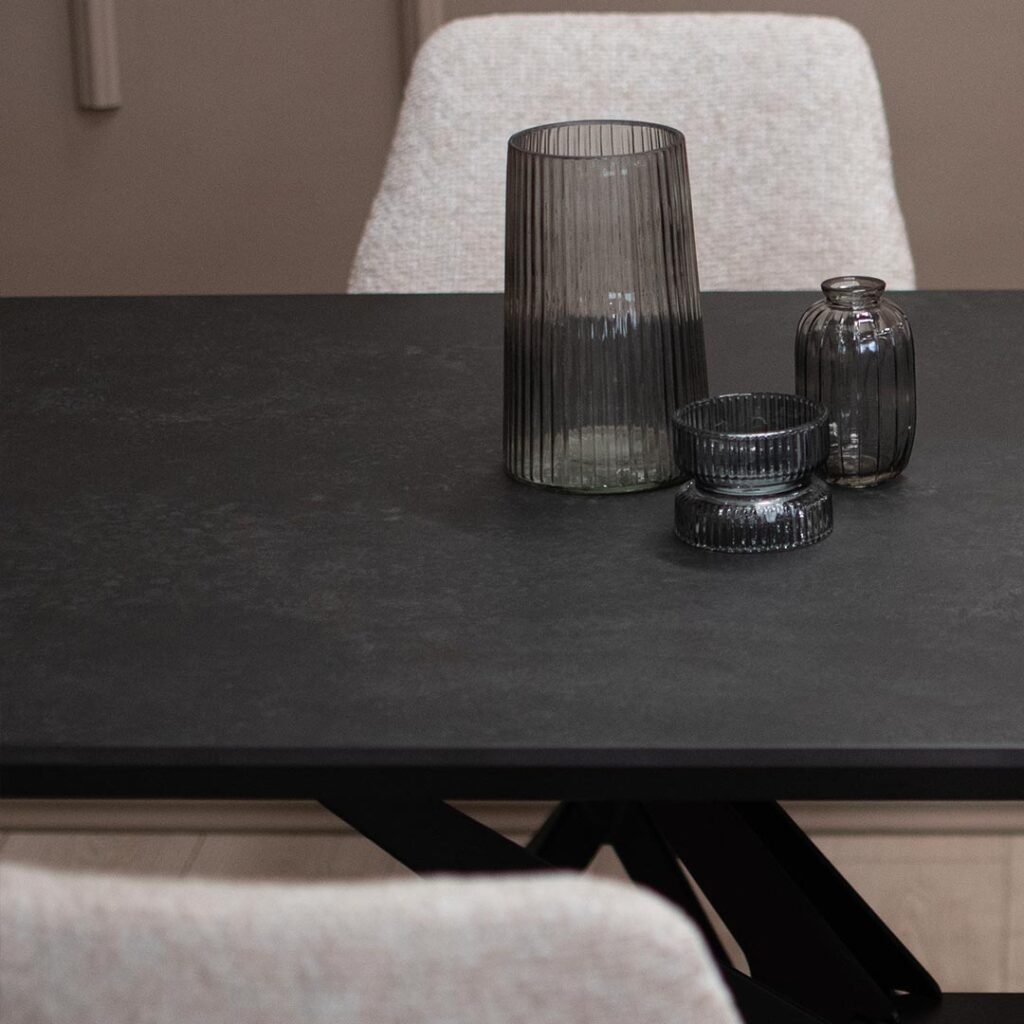 Трпезариска маса со црна керамичка плотна и метални ногарки во форма X.