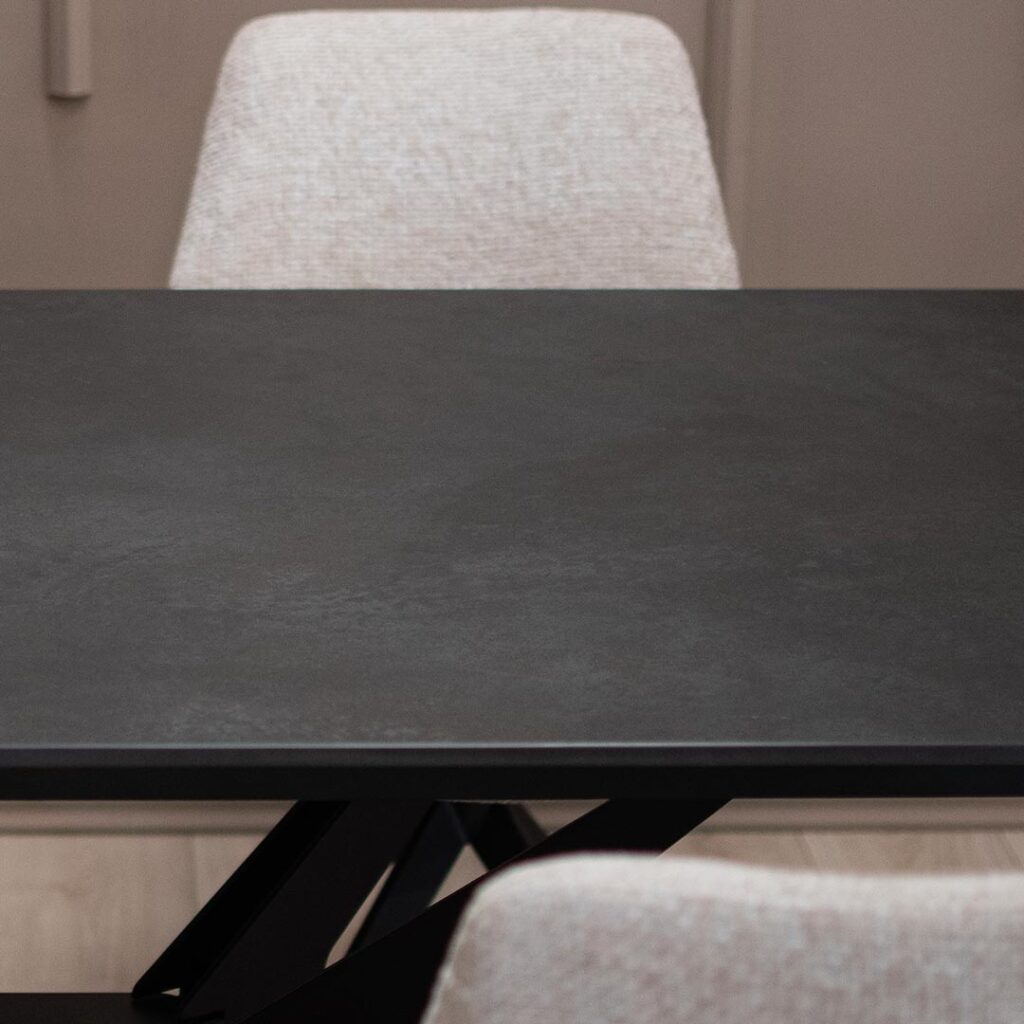 Трпезариска маса со црна керамичка плотна и метални ногарки во форма X.