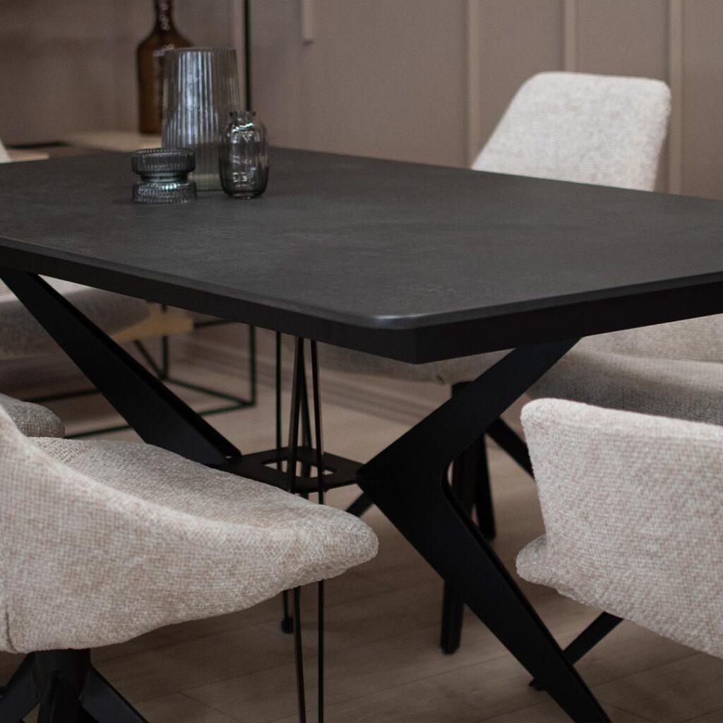 Трпезариска маса со црна керамичка плотна и метални ногарки во форма X.