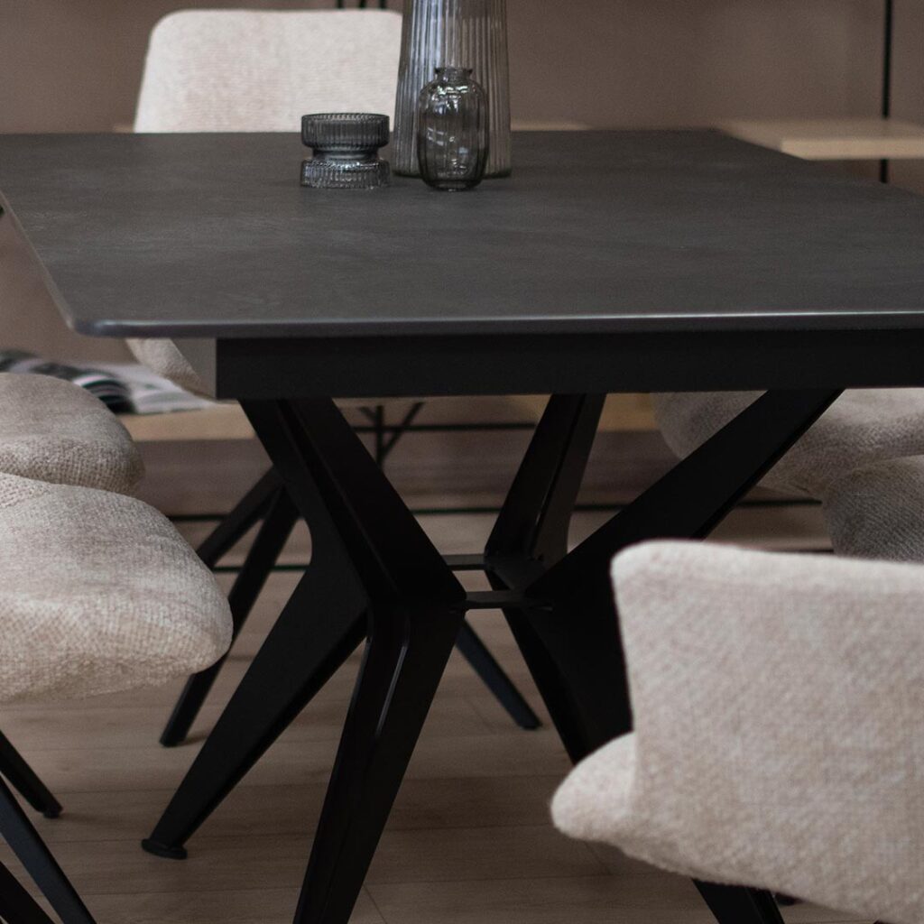Трпезариска маса со црна керамичка плотна и метални ногарки во форма X.