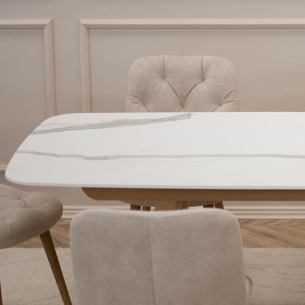 Трпезариски сет со маса со керамичка плотна и две дрвени со неправилна форма ногарки, во комбинација со 6 столици во крем велвет и дрвени даб ногарки.