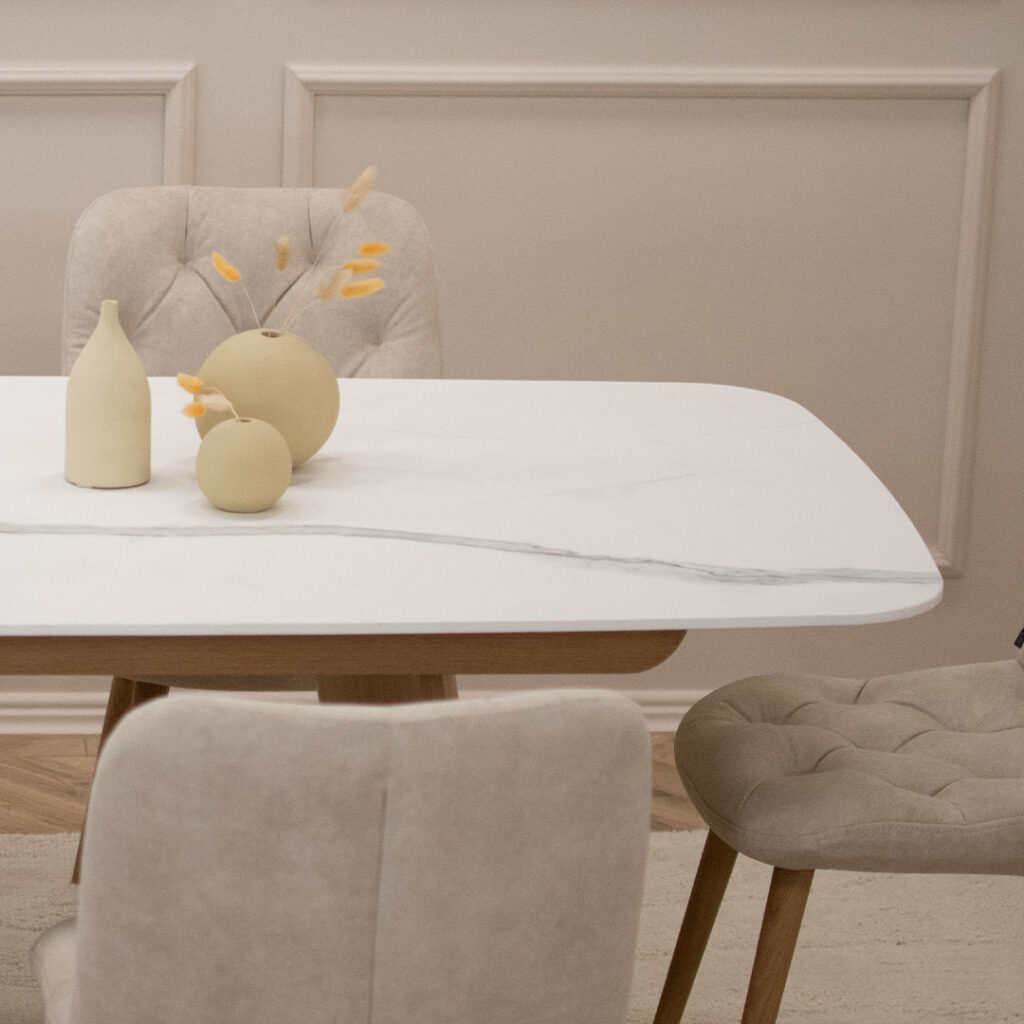 Трпезариски сет со маса со керамичка плотна и две дрвени со неправилна форма ногарки, во комбинација со 6 столици во крем велвет и дрвени даб ногарки.