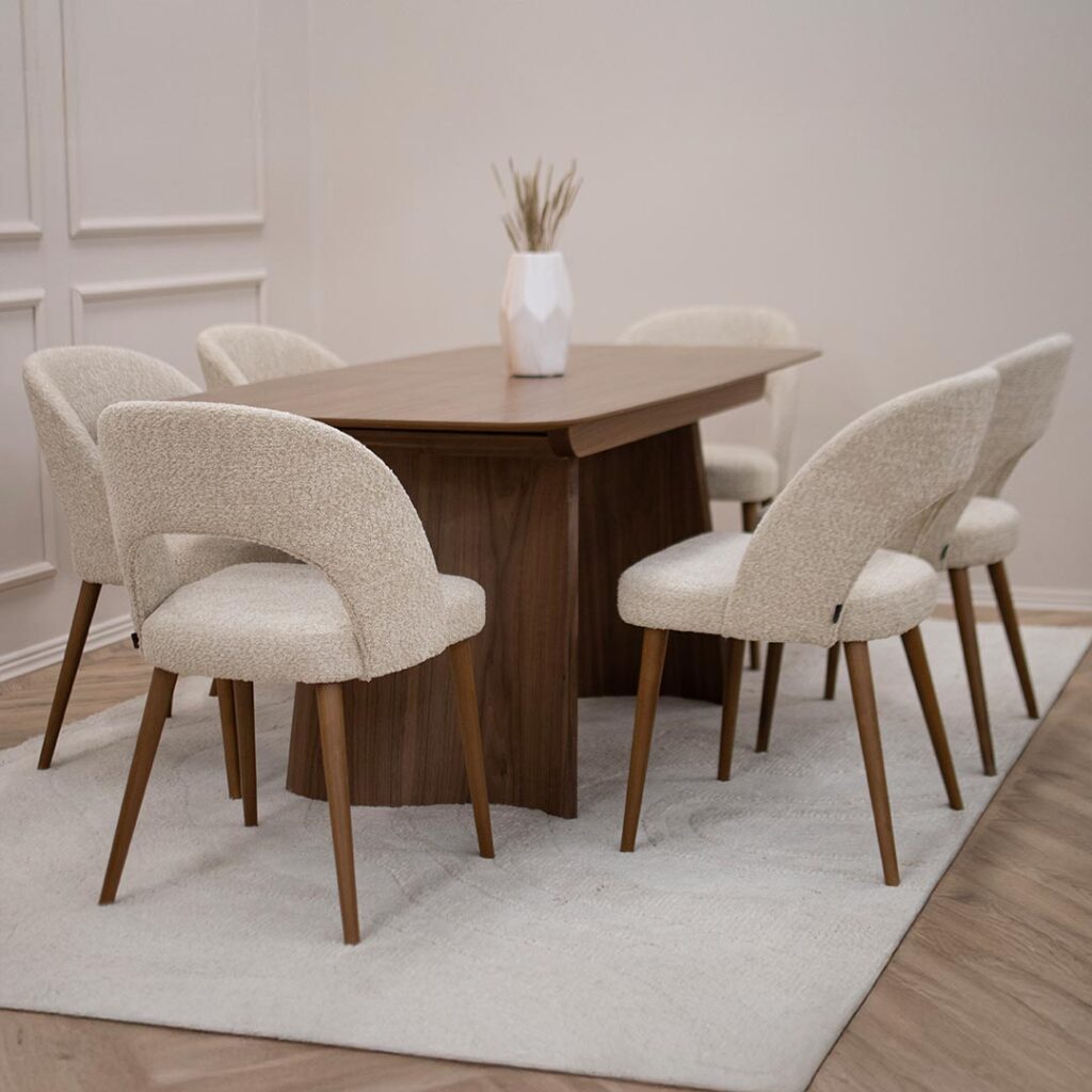 Трпезариски сет со трпезариска маса Сфера од орев со две неправилно обликувани дрвени ногарки со 6 трпезариски столици со бука кафеави ногарки и крем букле.