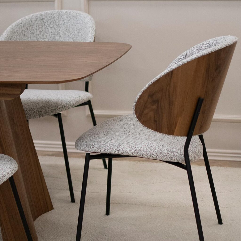 Трпезариска столица со грб од фурнир орев и светло крем мебел штоф, поставена на црни метални ногарки.