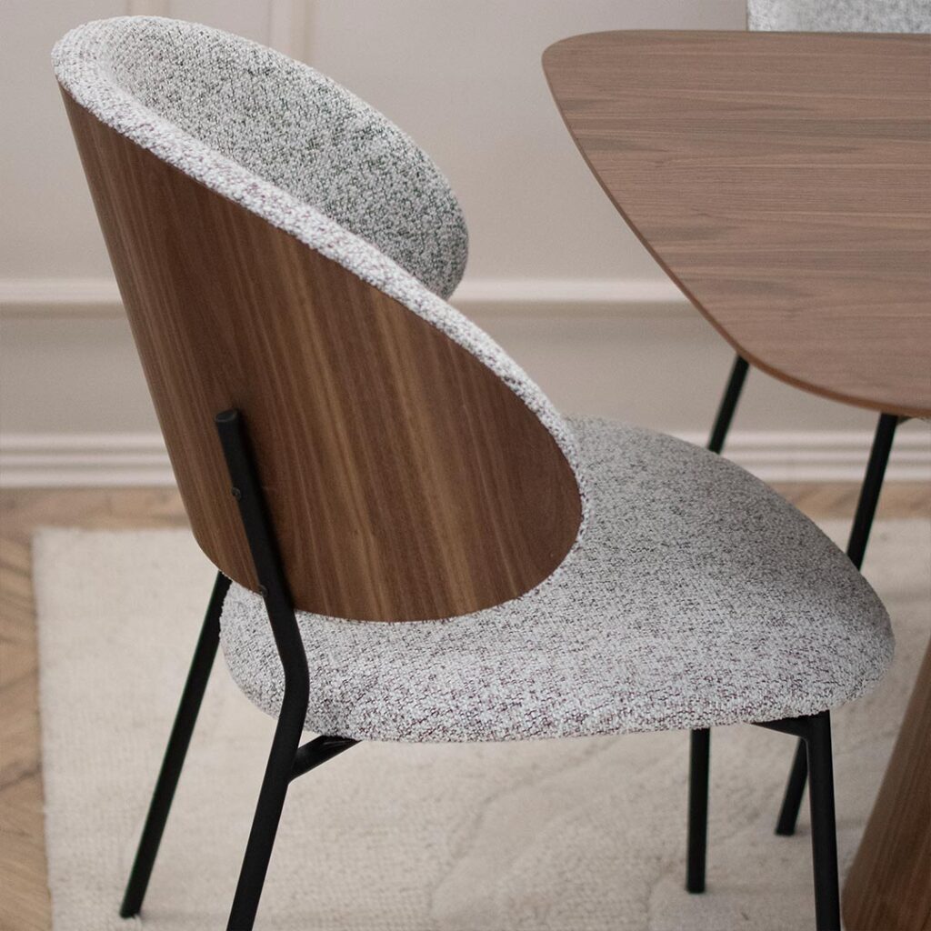 Трпезариска столица со грб од фурнир орев и светло крем мебел штоф, поставена на црни метални ногарки.