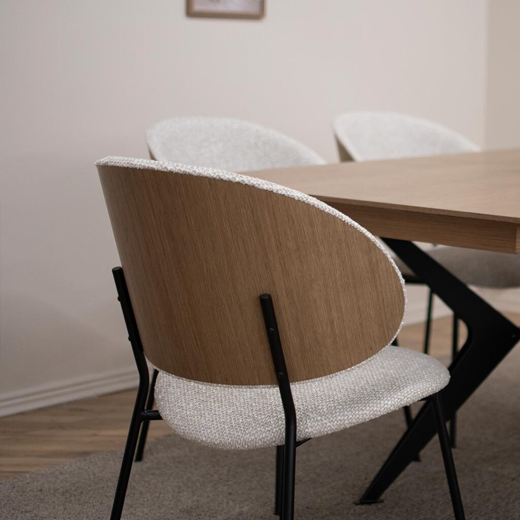 Трпезариска сролица, со удобно седло во беж мебел штоф и фурнир од даб во грбот, поставена на црни елегантни метални ногарки.