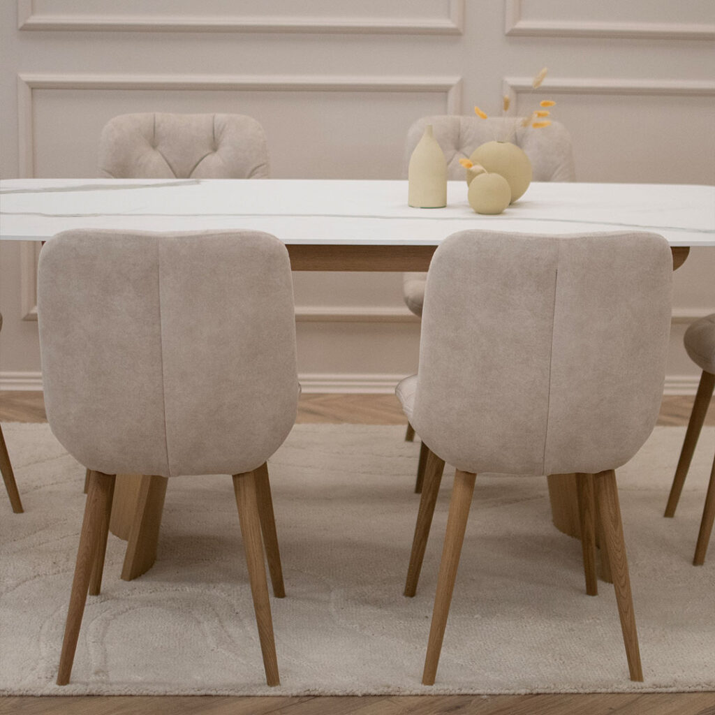 Трпезариски сет со маса со керамичка плотна и две дрвени со неправилна форма ногарки, во комбинација со 6 столици во крем велвет и дрвени даб ногарки.