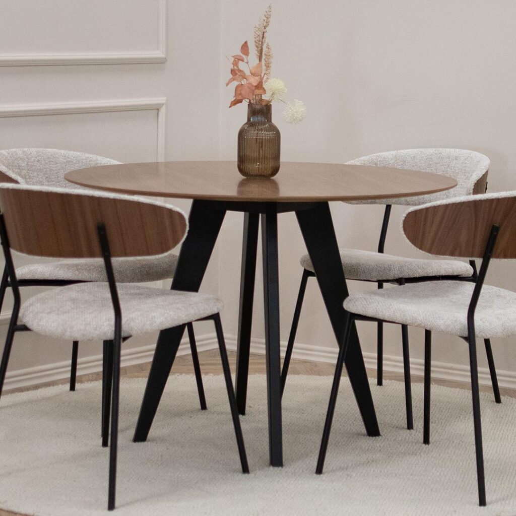 Мала кружна маса со плотна орев и црни ногарки, со 4 столици со метални ногарки и светло крем мебел штоф, кои на грб имаат фурнир од орев.