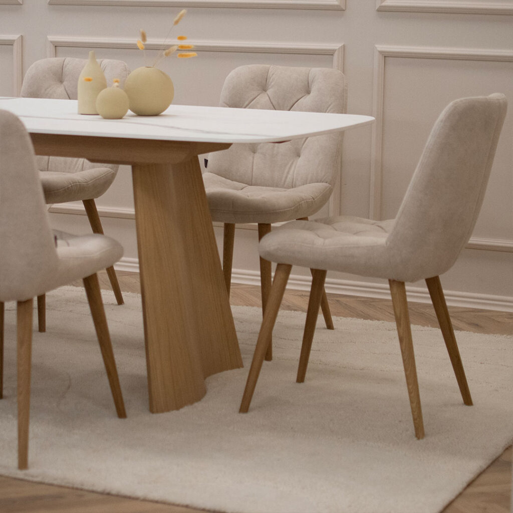 Трпезариски сет со маса со керамичка плотна и две дрвени со неправилна форма ногарки, во комбинација со 6 столици во крем велвет и дрвени даб ногарки.