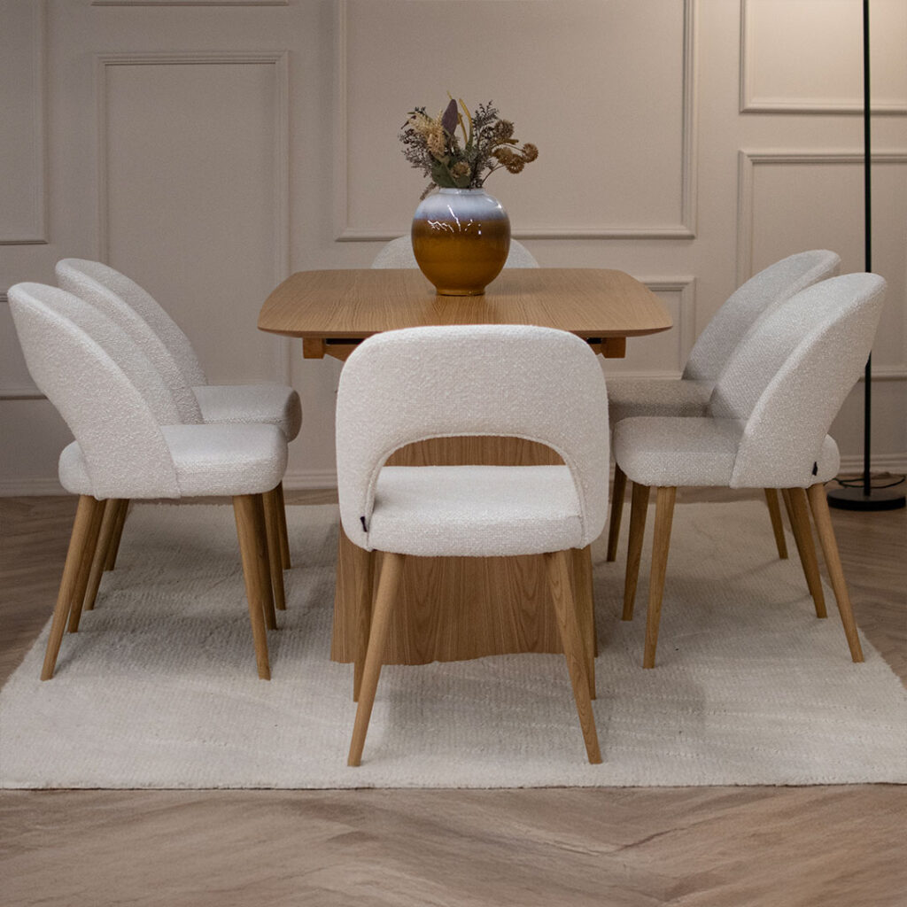 Трпезариски сет со маса Сфера од маслен даб со две неправилно обликувани ногарки во комбинација со 6 столици со даб ногарки и бел мебел штоф.