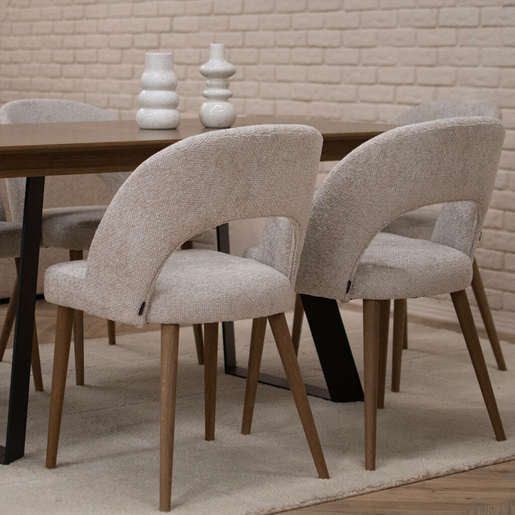 Трпезариски столици, со отвор во грб, изработени во беж мебел штоф и дрвени даб ногарки кои одговараат на плотната на трпезариската маса.