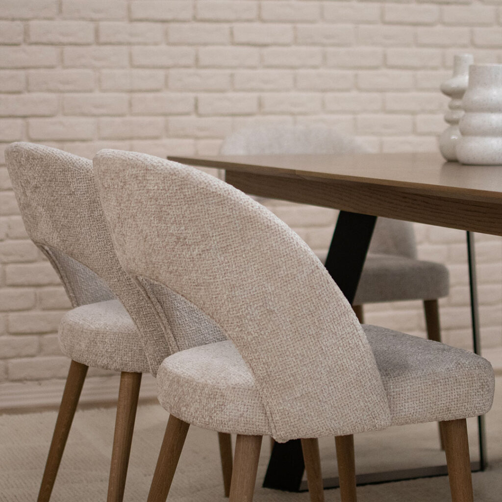 Трпезариски столици, со отвор во грб, изработени во беж мебел штоф и дрвени даб ногарки кои одговараат на плотната на трпезариската маса.