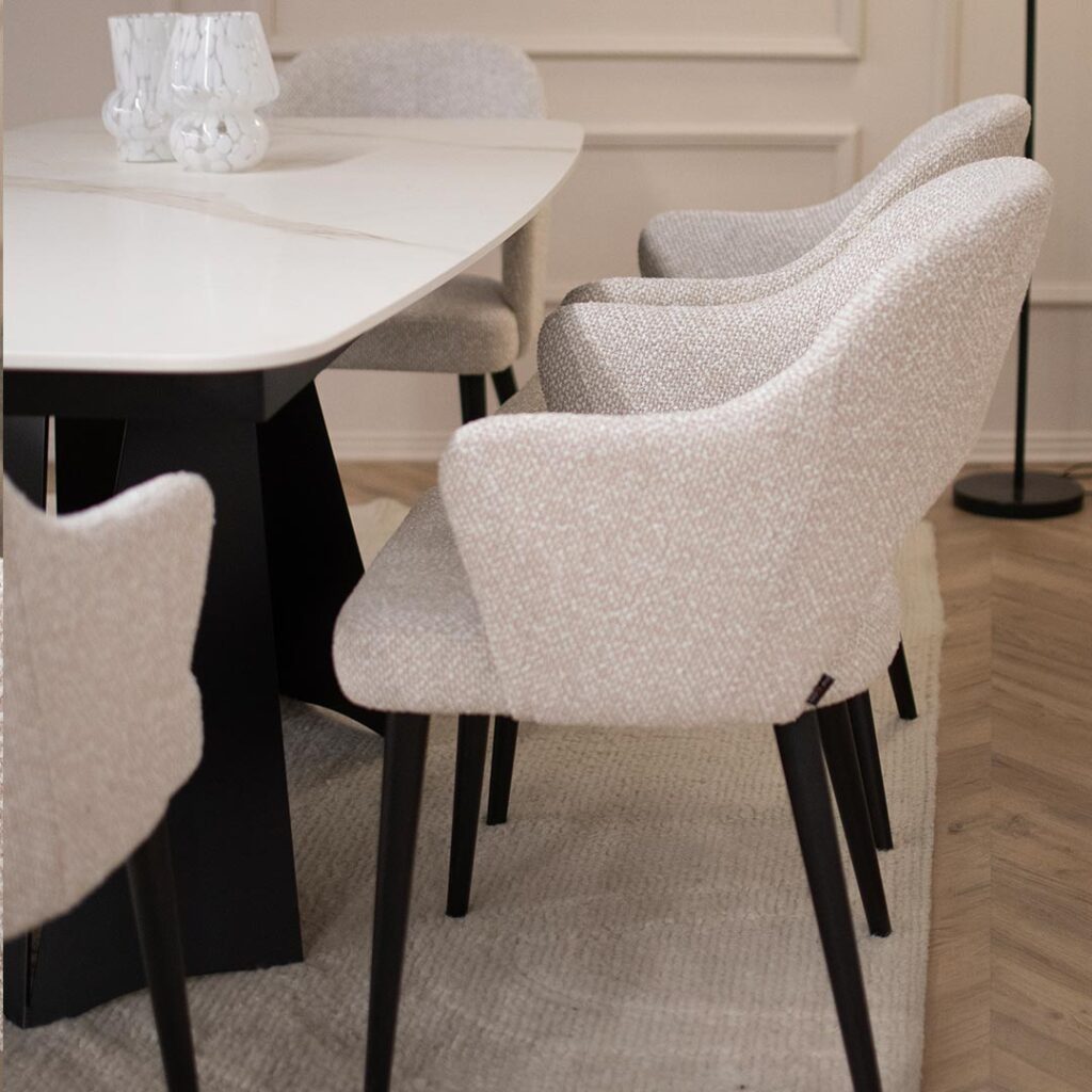 Трпезариска маса со керамичка плотна во бела боја со крем шари поставена на две црни метални ногарки во комбинација со столици со раконаслон во бел мебел штоф со црни дрвени ногарки.