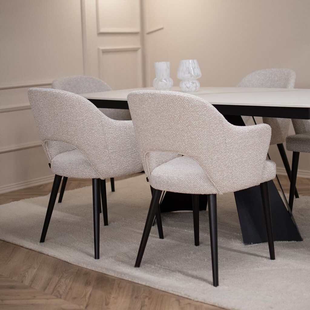 Трпезариска маса со керамичка плотна во бела боја со крем шари поставена на две црни метални ногарки во комбинација со столици со раконаслон во бел мебел штоф со црни дрвени ногарки.