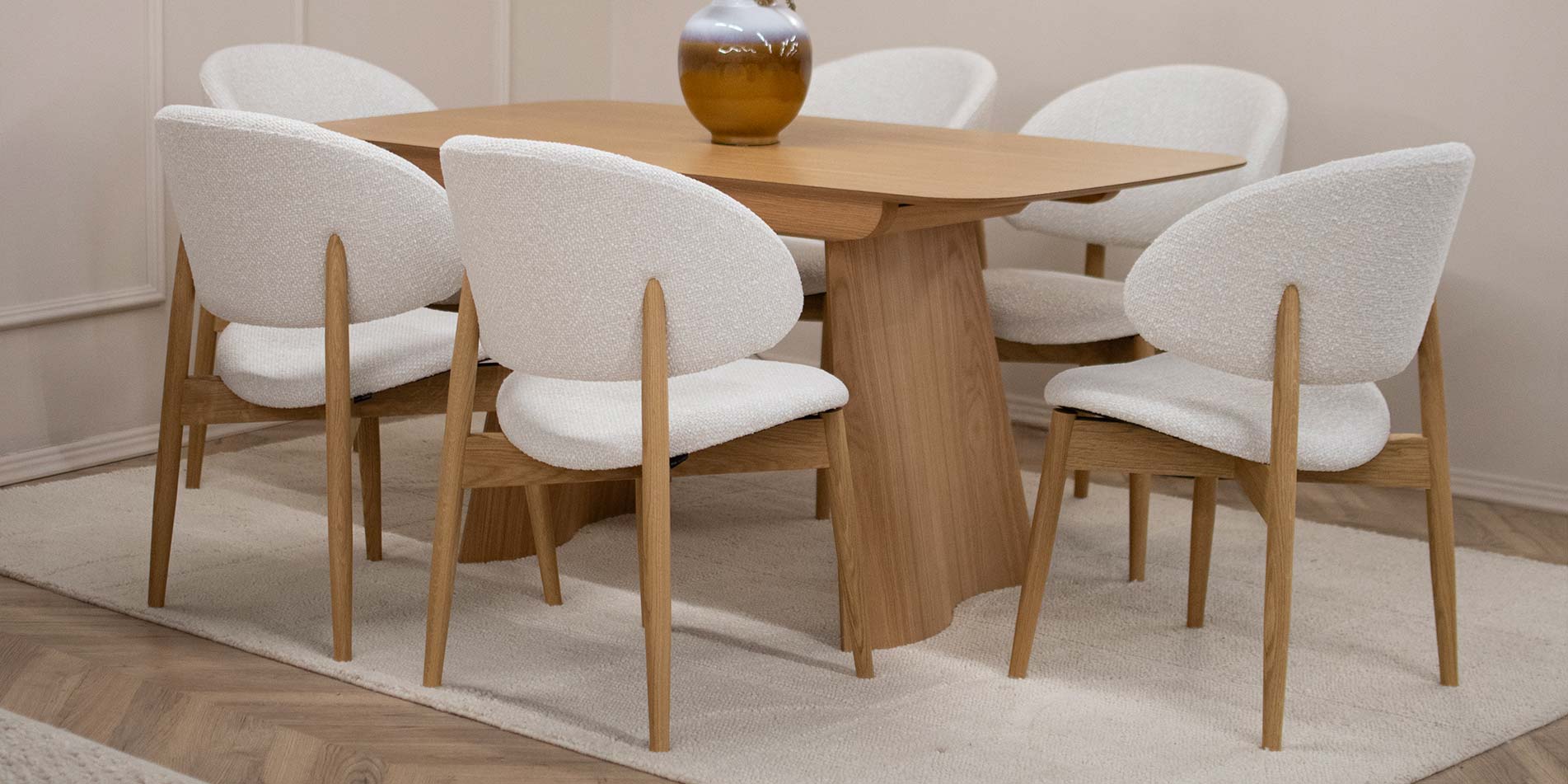 Трпезариска столица Celine со даб ногарки со светло крем мебел штоф, поставени на маса од дрво даб натур.