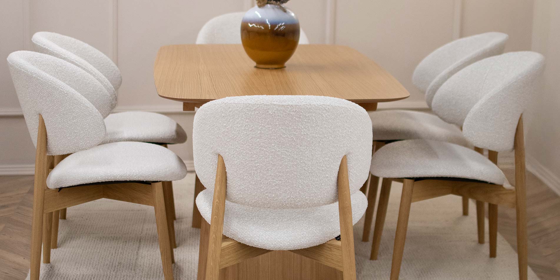 Трпезариска столица Celine со даб ногарки со светло крем мебел штоф, поставени на маса од дрво даб натур.