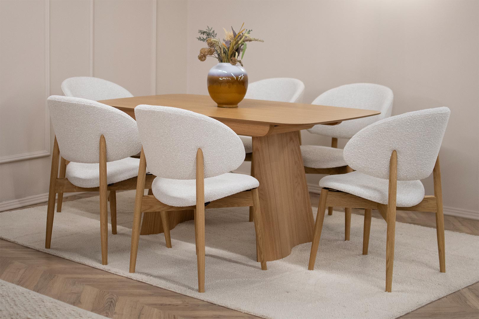 Трпезариски сет со маса од дрво даб со заоблени агли и две неправилна форма ногарки, со трпезариски столици во бел мебел штоф и даб натур боја ногарки.