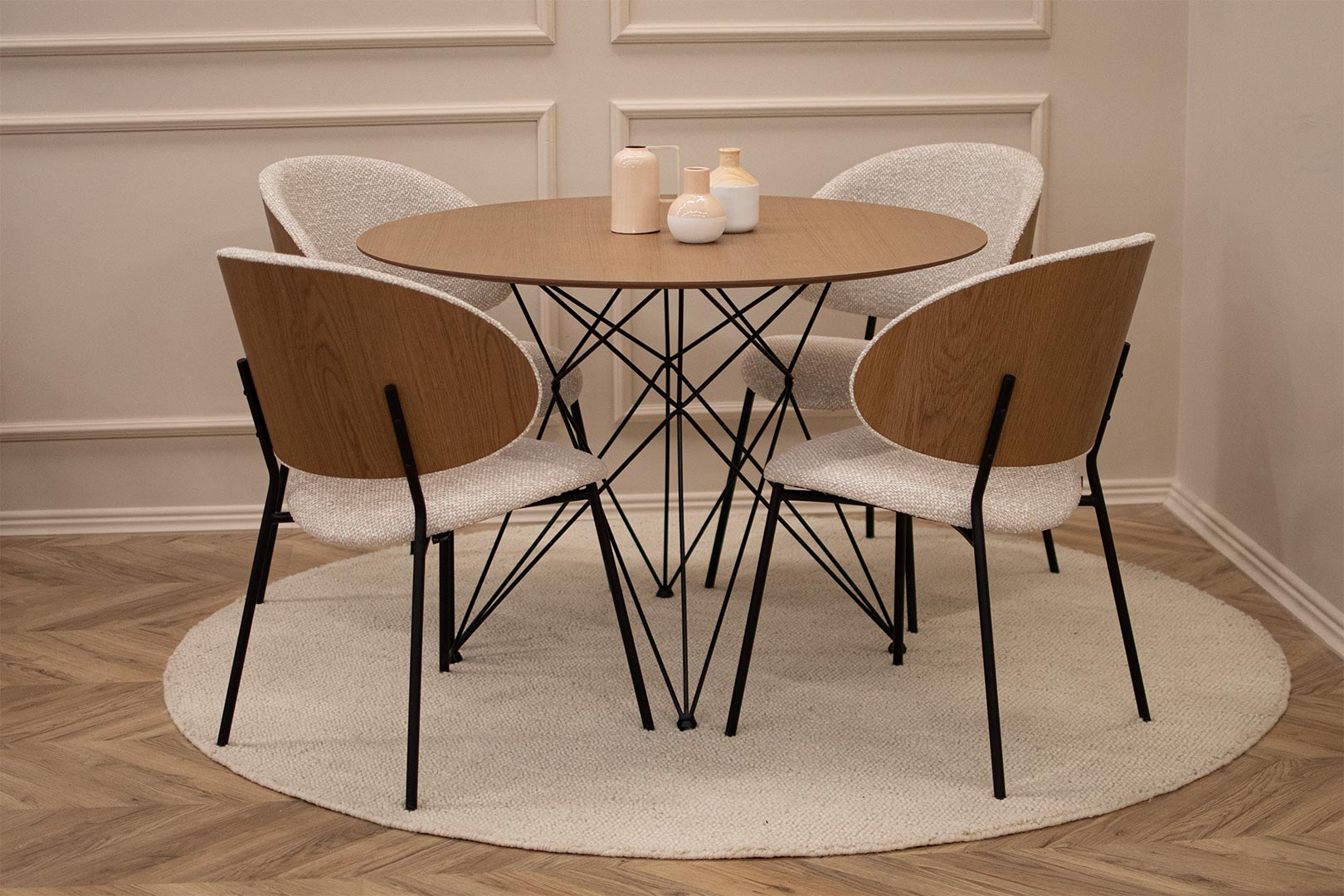 Трпезариски сет со мала кружна маса со плотна дурниран медијапан даб во кафеава нијанса и црни испреплетени метални ногарки, со 4 трпезариски столици со грб од фурнир даб во комбинација со крем мебел штоф и црни метални ногарки.