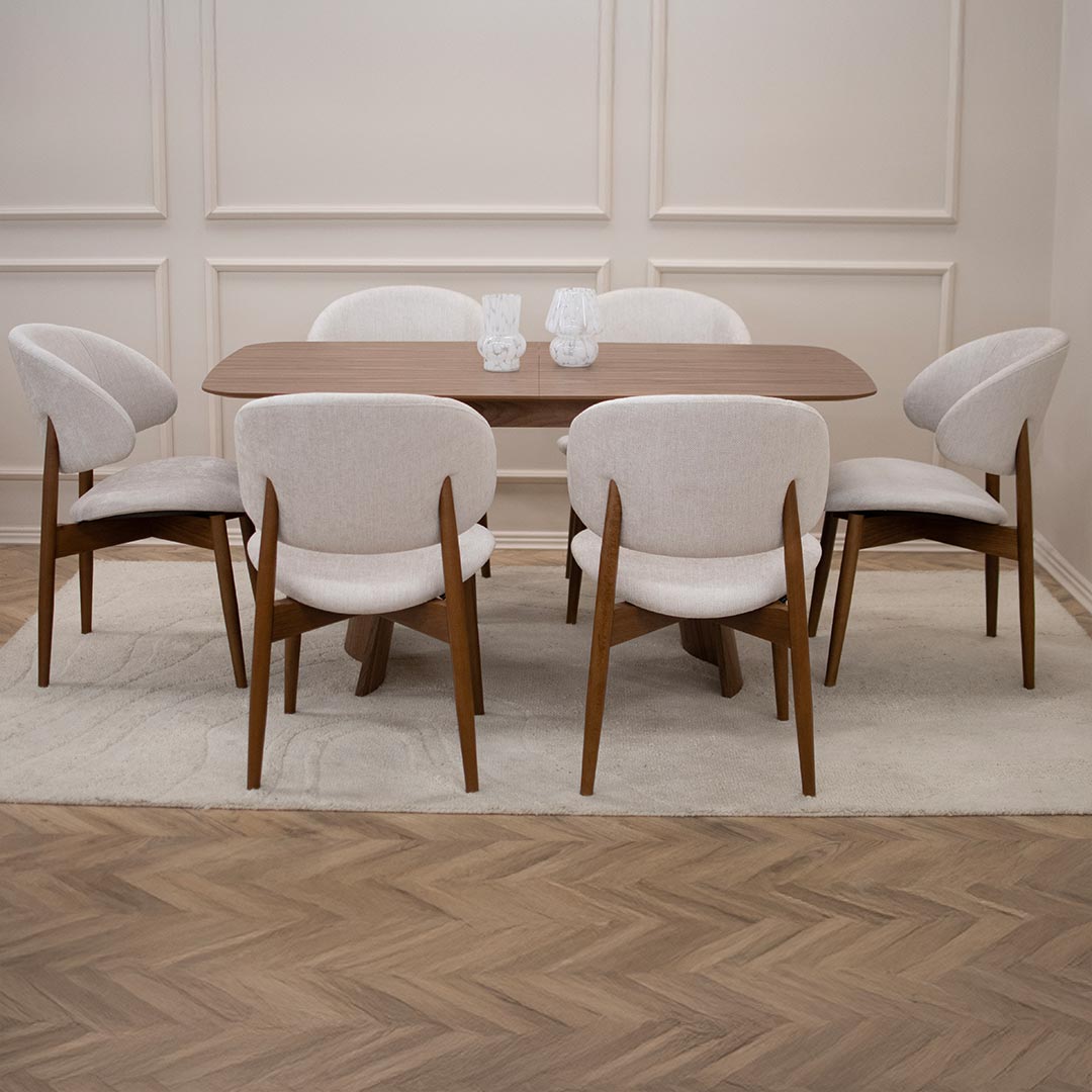 Трпезариска столица Celine со бука ногарки со светло крем мебел штоф, поставени на маса од дрво орев.