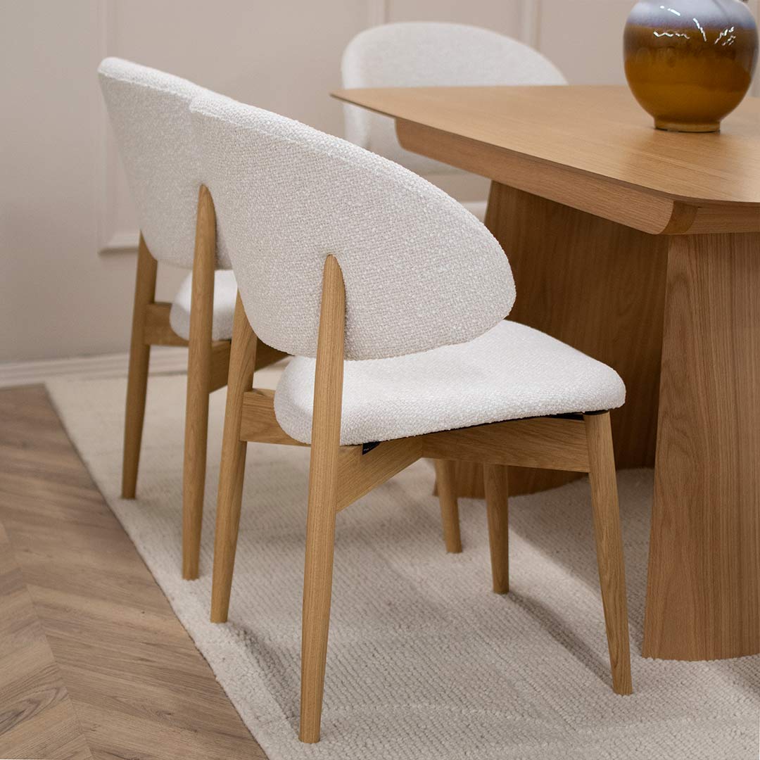 Трпезариска столица Celine со даб ногарки со светло крем мебел штоф, поставени на маса од дрво даб натур.