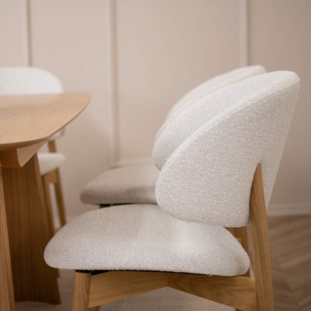 Трпезариска столица Celine со даб ногарки со светло крем мебел штоф, поставени на маса од дрво даб натур.