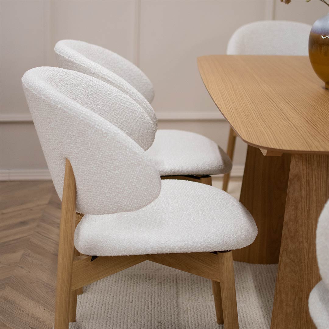 Трпезариска столица Celine со даб ногарки со светло крем мебел штоф, поставени на маса од дрво даб натур.