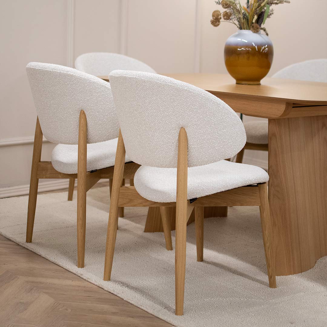 Трпезариска столица Celine со даб ногарки со светло крем мебел штоф, поставени на маса од дрво даб натур.