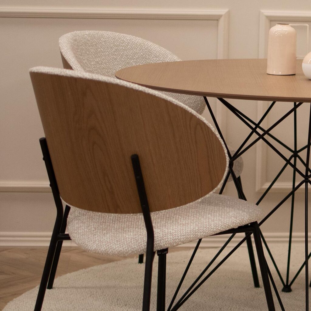 Трпезариски столици со грб од фурнир даб во комбинација со крем мебел штоф и црни метални ногарки.